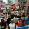 dzieci_siedza_na_poduszkach_sluchaja_bajki_czytanej_przez_Pania_bibiotekarke